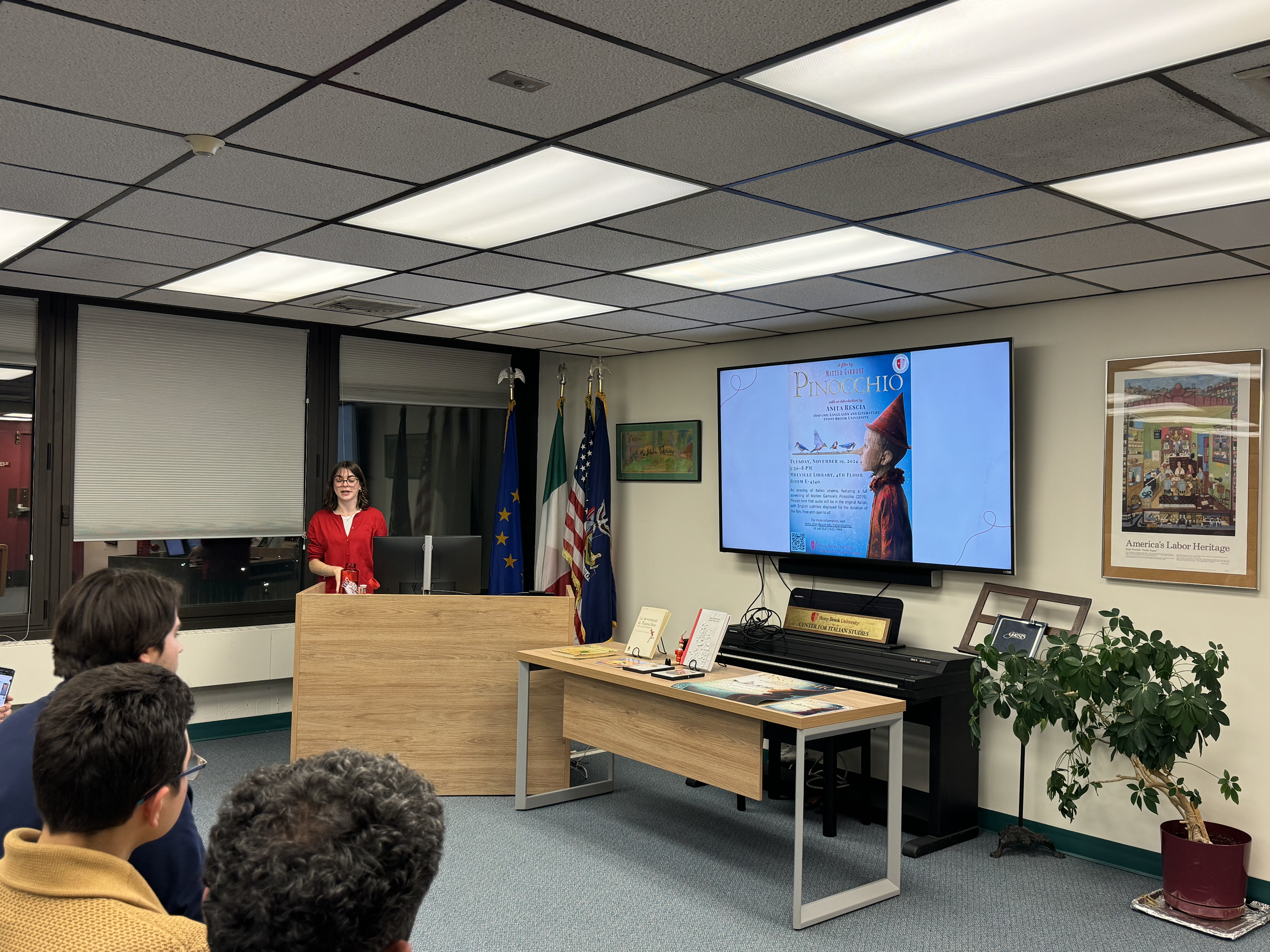 Anita Rescia giving a presentation on Pinocchio at the Center. There is a slideshow on the TV and some people are sitting in attendance