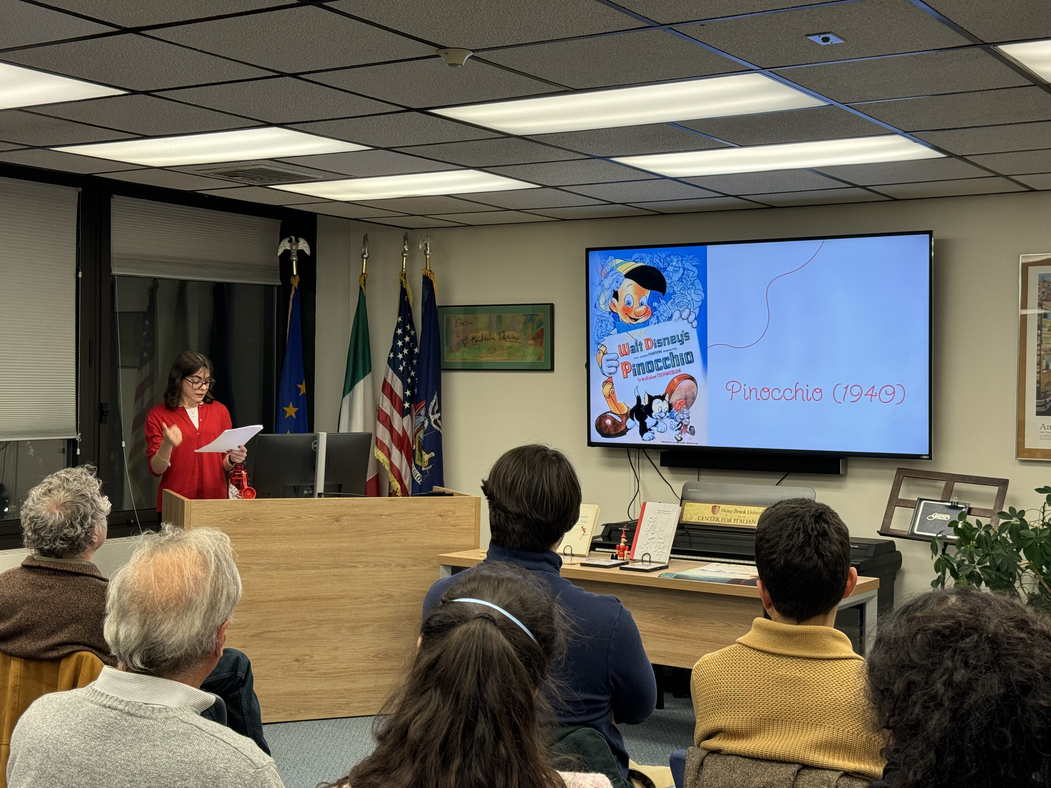 Anita Rescia giving a presentation on Pinocchio at the Center. There is a slideshow on the TV and some people are sitting in attendance