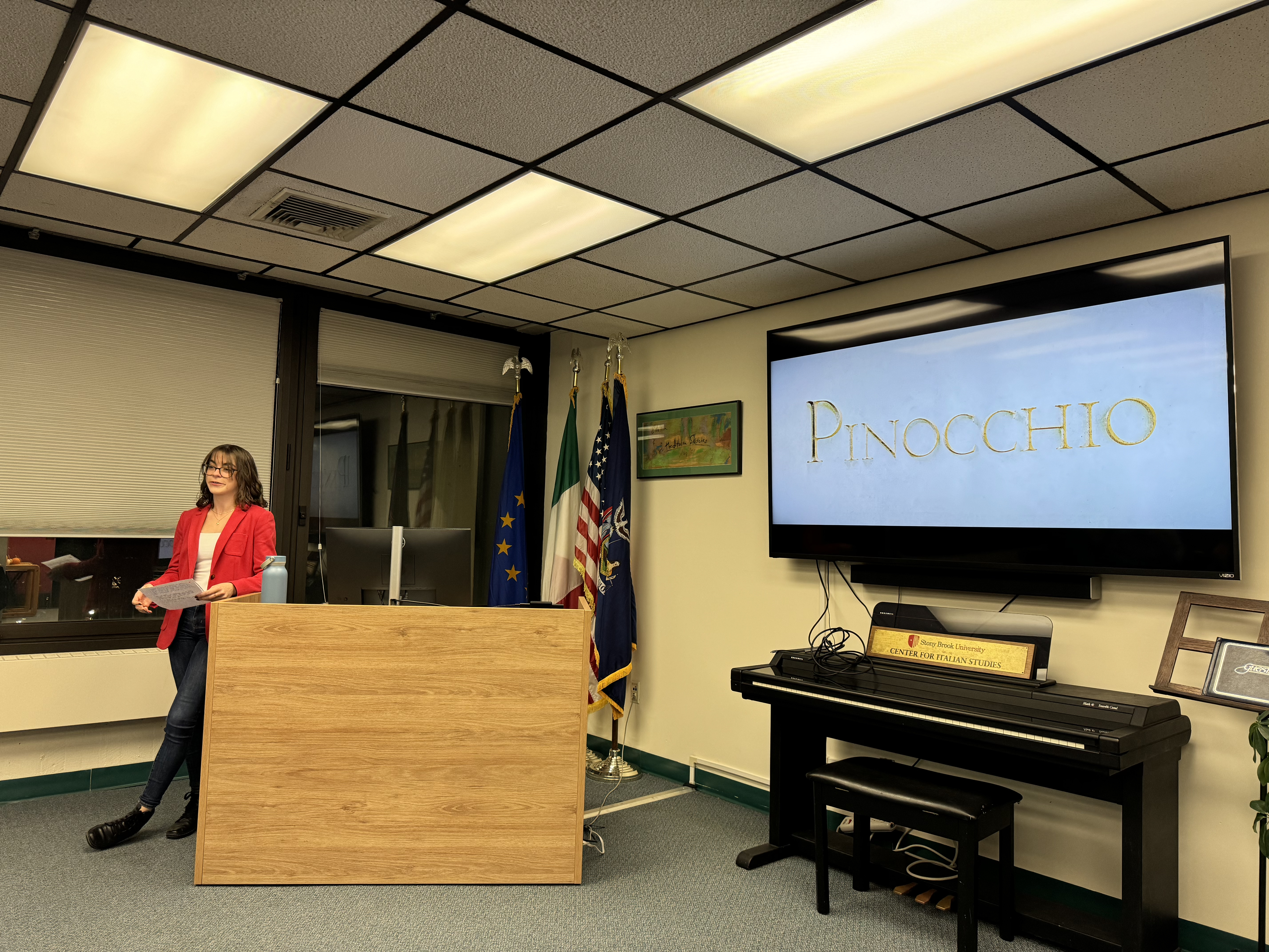 Anita Rescia giving a presentation on Pinocchio at the Center. There is a slideshow on the TV and some people are sitting in attendance