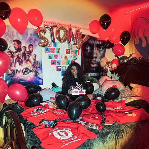 A student in their dorm room that is decorated with Stony Brook apparel and red balloons
