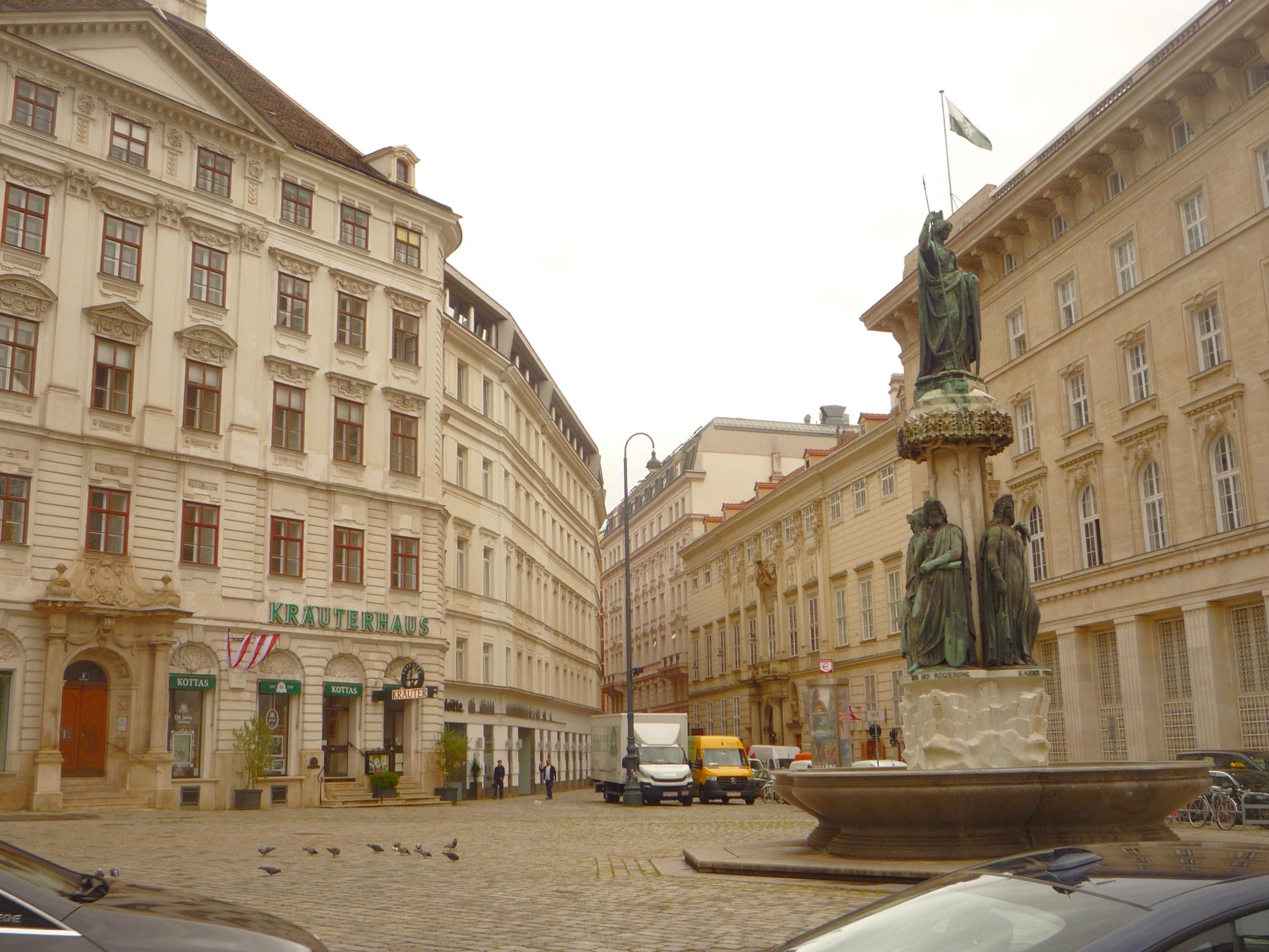 Judenplatz in Vienna View of Judenplatz in Vienna, featuring the Lessing Monument, surrounded by classic European buildings and parked vehicles. Pigeons are scattered across the cobblestone square.