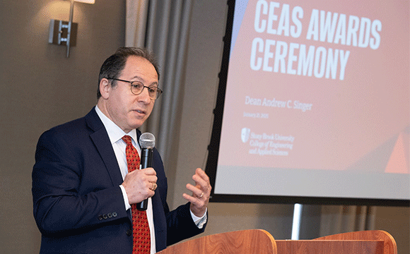 Dean Andrew Singer A man in a suit speaks at a podium with a microphone, gesturing with one hand. A presentation slide titled "CEAS Ceremony" is visible in the background.