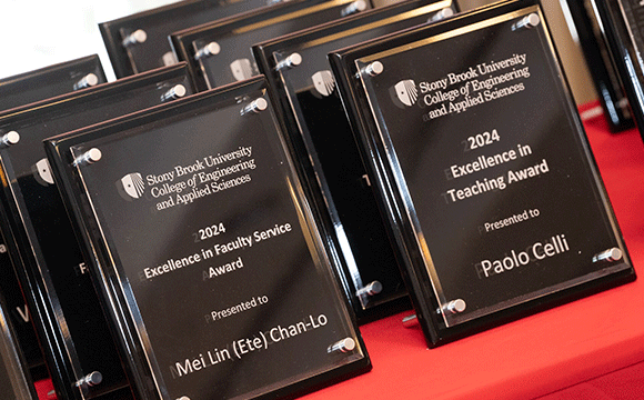 Excellence in Mentorship Multiple black plaques with silver text titled "Stony Brook University College of Engineering and Applied Sciences," highlighting awards for Excellence in Faculty Service and Teaching for 2024, displayed on a red cloth.
