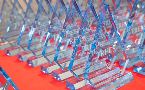 TREES Awards A row of transparent, blue-tinted glass awards shaped like elongated diamonds stand on a vivid red tablecloth, conveying a sense of celebration and achievement.